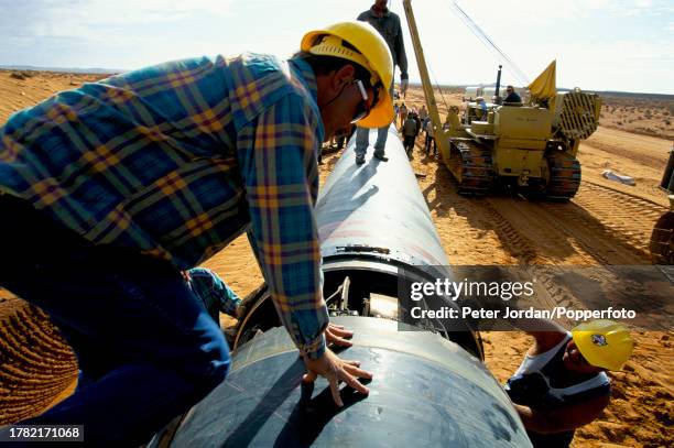 Expatriate American workers from Bechtel Corporation work together with local workers to join up pipe sections during construction of the...