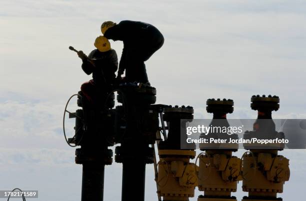 Two workers, wearing Bechtel Corporation hard hats, tighten bolts on pipework valves during construction of the Maghreb-Europe Gas Pipeline in the...
