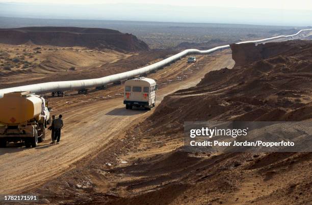 Bus drives by sections of completed pipework waiting to be buried underground during construction of the Maghreb-Europe Gas Pipeline in the desert...