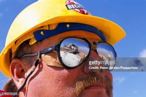 Wearing mirror shaded sunglasses, an expatriate American worker from Bechtel Corporation works together with local workers to join up pipe sections...