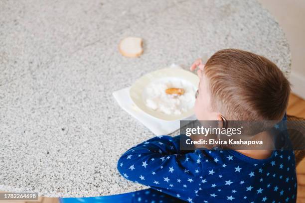 9-year-old boy has breakfast with rice porridge and nuggets with a hearing aid in his ear, top view. the life of a hearing-impaired child - eating nuggets ストックフォトと画像