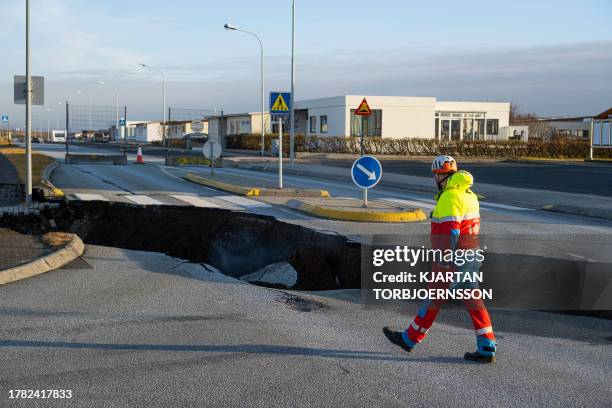 This photo taken on November 13, 2023 shows a member of the emergency services walking near a crack cutting across the main road in Grindavik,...