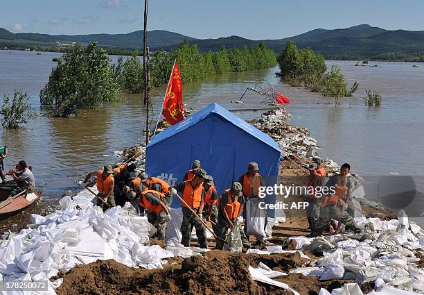 Rescuers work on a flood control dam in front of a street submerged by flood water in Tongjiang, northeast China's Heilongjiang province on August...