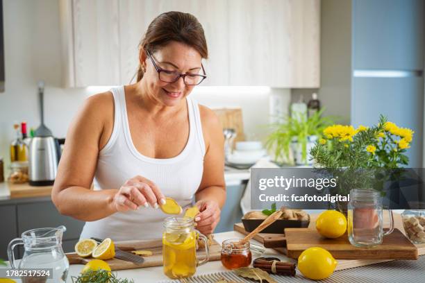femme mûre préparant de l’eau infusée au gingembre et au citron - antioxydant photos et images de collection