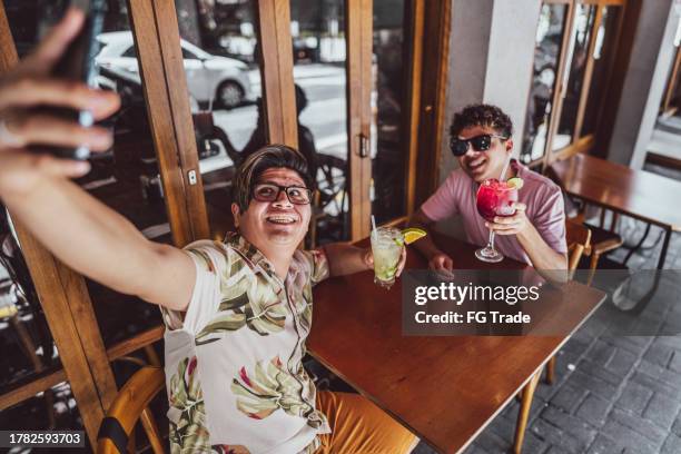 touristisches schwules paar, das ein selfie mit dem handy im restaurant macht - caipirinha stock-fotos und bilder