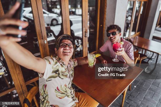 tourist gay couple taking a selfie using mobile phone at restaurant - caipirinha stock pictures, royalty-free photos & images