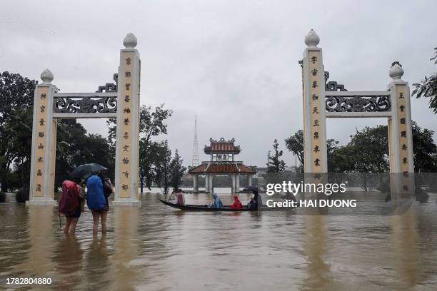 People ride on a boat and walk through a flooded area of Hue city in central Vietnam on November 15, 2023. Two people died and three were missing...