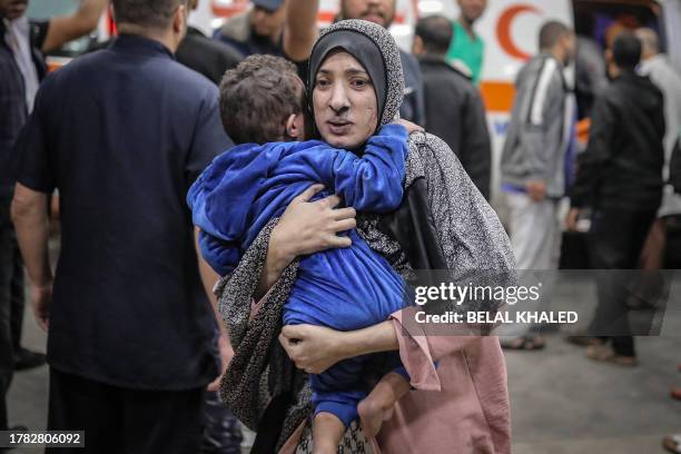 Palestinian woman covered in dust rushes with her child in her arms into the hospital following the Israeli bombardment of Khan Yunis in the southern...