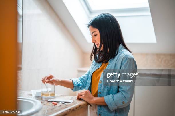 asiatische frau, die schwangerschaftstest zu hause durchführt - urine sample stock-fotos und bilder