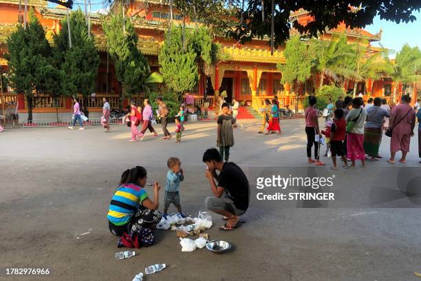 People eat food at a monastery-turned-temporary shelter for internally displaced people in Lashio, Shan state on November 15, 2023. Fighting has...