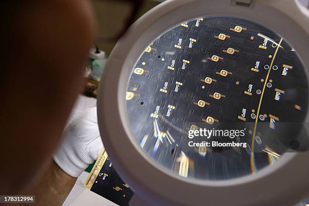 An employee uses a magnifying glass to inspect a Flexible Printed Circuit Board panel on the production line at the Seil Electronics Co. Factory in...