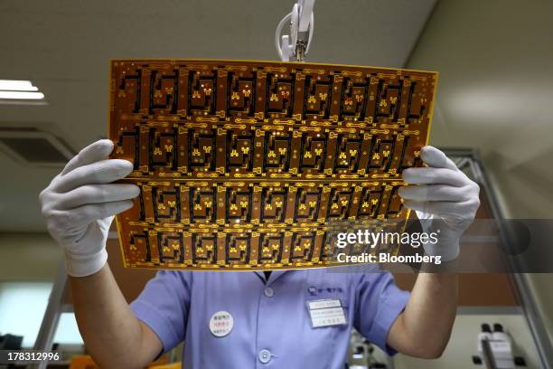 An employee uses a magnifying glass to inspect a Flexible Printed Circuit Board panel on the production line at the Seil Electronics Co. Factory in...