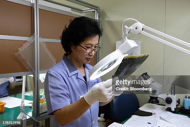 An employee uses a magnifying glass to inspect a Flexible Printed Circuit Board panel on the production line at the Seil Electronics Co. Factory in...