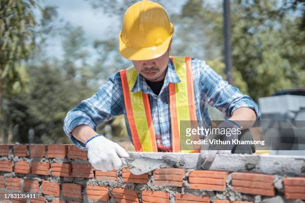 bricklayer worker installing bricks on construction site, exterior wall of building. - ouvrier maçon photos et images de collection