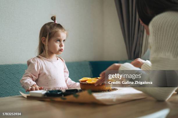 young mother scolds her offended daughter at table in the kitchen at home - streiten stock-fotos und bilder
