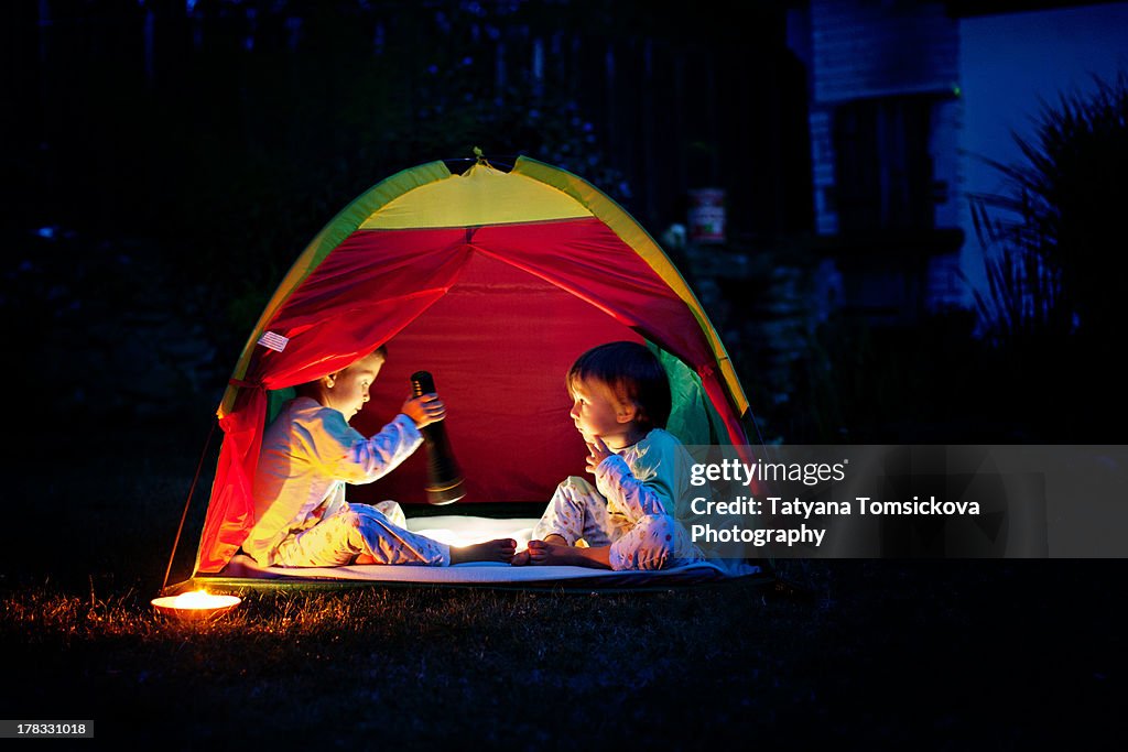 Two boys in a tent at night, reading a book