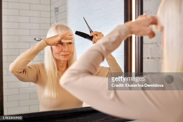 elderly woman cuts her bangs at home in front of the bathroom mirror - older woman colored hair stock pictures, royalty-free photos & images