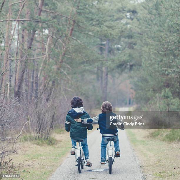 two boys on bikes on a tree lane - familie fietsen close up stockfoto's en -beelden