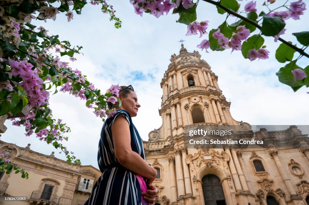 Beautiful woman under the flower branch, visiting Modica, Sicily travel 2023.