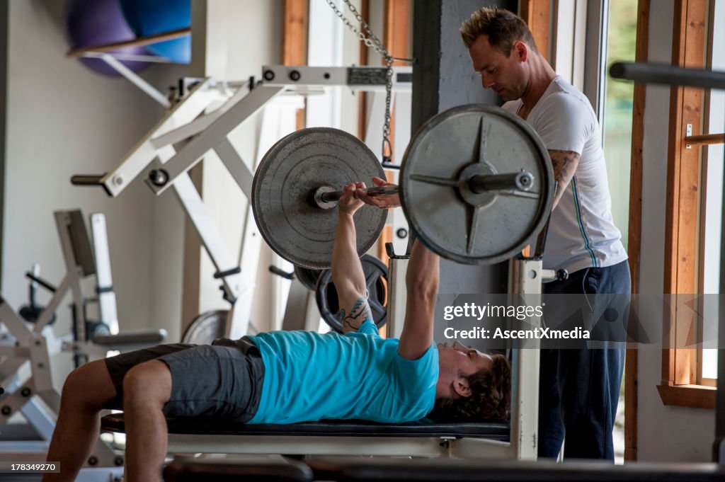 Trainer provides assistance to man lifting weights