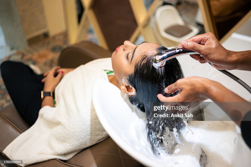Young woman enjoying while getting her hair washed by professional hairdresser at salon