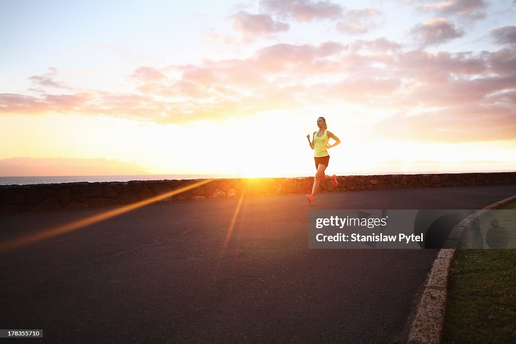 Girl running on road near ocean at sunset