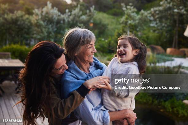 kleines mädchen lacht, während es mit seiner großmutter und mutter im freien steht - familie mit mehreren generationen stock-fotos und bilder