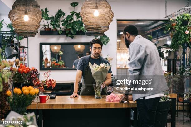 male customer buying a flower bouquet from local flower shop - flower shop stock pictures, royalty-free photos & images