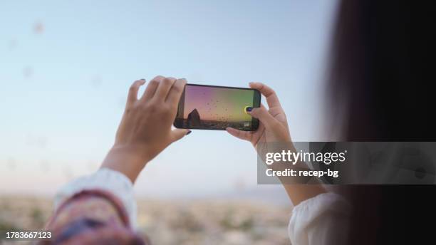 young female tourist taking photos of hot air ballons from balcony of hotel during her travel - göreme national park stock pictures, royalty-free photos & images