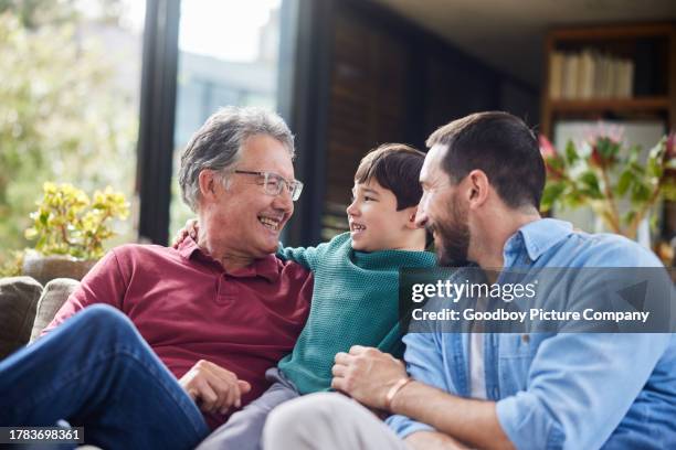 little boy sitting with his dad and grandfather on a living room sofa - grandpa son stock pictures, royalty-free photos & images