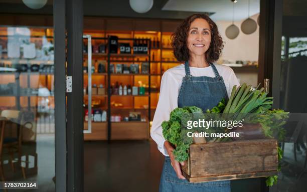lächelnde besitzerin steht mit einer kiste mit produkten vor ihrem laden - grocer stock-fotos und bilder