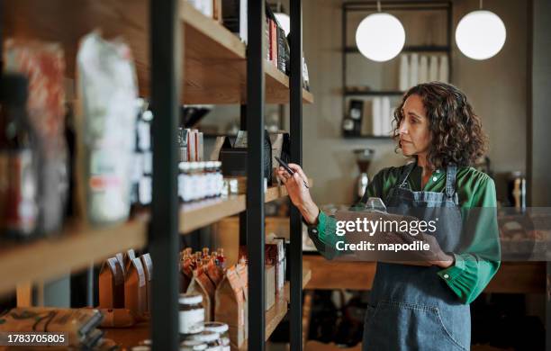 propietario maduro de delicatessen que hace inventario en los estantes de la tienda usando un portapapeles - hacer inventario fotografías e imágenes de stock