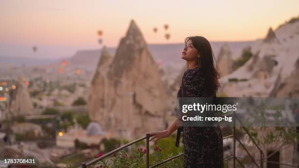 portrait of young female tourist watching hot air ballons from balcony in cappadocia during her travel - göreme national park stock pictures, royalty-free photos & images