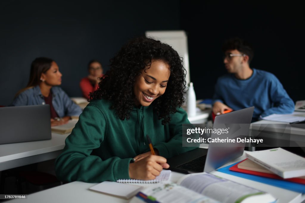 A female student smiling as she writes on a notebook in a classroom.