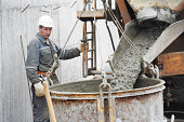 Builder worker pouring concrete into barrel