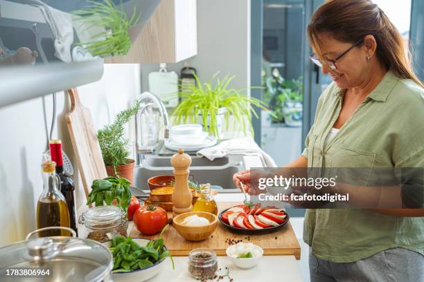mature woman dressing caprese salad with pesto sauce - pesto sauce stock pictures, royalty-free photos & images