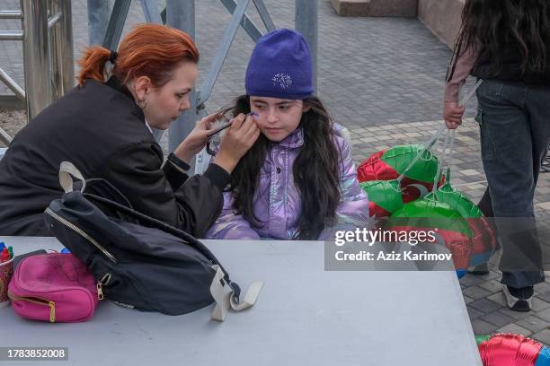 Young girl paints Azerbaijan flag to kids face on November 9, 2023 in Baku, Azerbaijan. The three-color flag with a crescent and an eight-pointed...