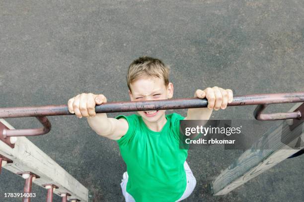 little boy doing chin-up on the horizontal bar - aspiration and persistence during children's sports exercise on the sport field - boys in pullups stockfoto's en -beelden