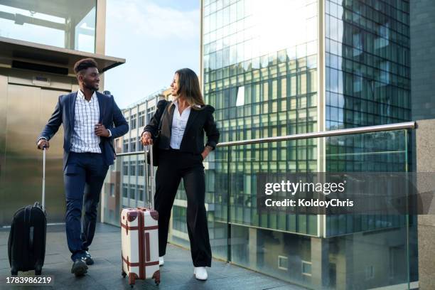 business professionals walking together in modern cityscape with luggage - associate producer stock pictures, royalty-free photos & images