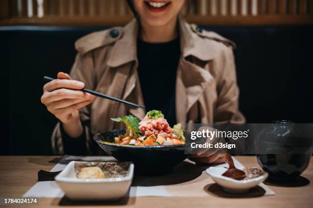 mid-section of smiling young asian woman can't wait to dig into her fresh sashimi rice bowl, chirashi don in a japanese restaurant. asian cuisine and food culture. foodie. experiential travel and vacation. people, food and lifestyle - experiential vacations stock pictures, royalty-free photos & images