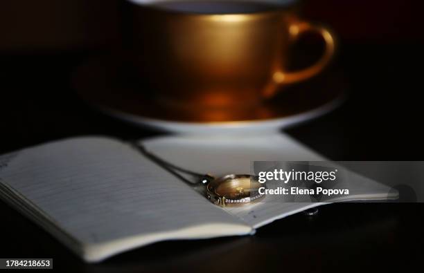 white gold chain necklace looks like compass against golden colored tea cup and diary paper - pendant stock pictures, royalty-free photos & images