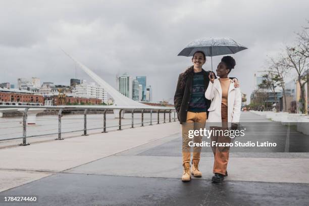 young couple walking using umbrella in puerto madero, buenos aires - puerto stock pictures, royalty-free photos & images