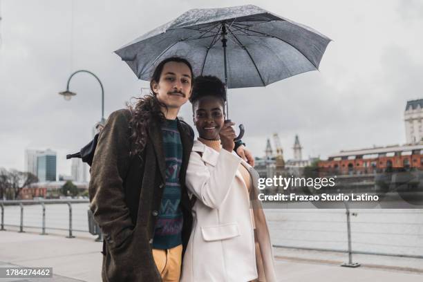 portrait of a young couple walking using umbrella in puerto madero, buenos aires - puerto stock pictures, royalty-free photos & images