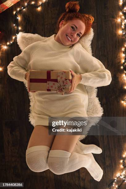 a happy smiling young woman holds a gift box in a cozy christmas atmosphere - models in stockings stock pictures, royalty-free photos & images