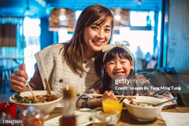 mom & daughter smiling joyfully at the camera while enjoying meal in a japaneses restaurant - noodle soup stock pictures, royalty-free photos & images