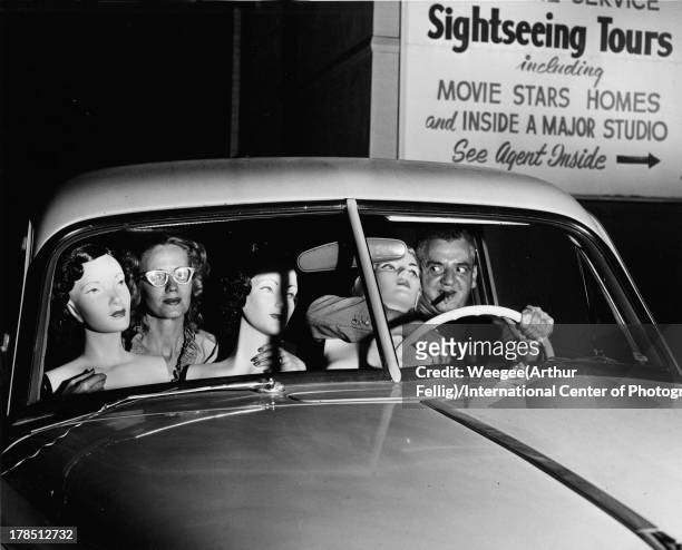 American photographer Weegee and an unidentified woman sit in the front seat of a car with a trio of mannequins, ca. 1950.
