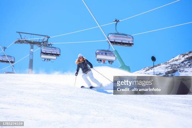 active lifestyle, vital female snow skier skiing, enjoying on sunny ski resorts. skiing carving at high speed against blue sky. - skipiste stockfoto's en -beelden