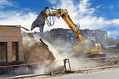 Building demolition machine pulls down a wall on a sunny day