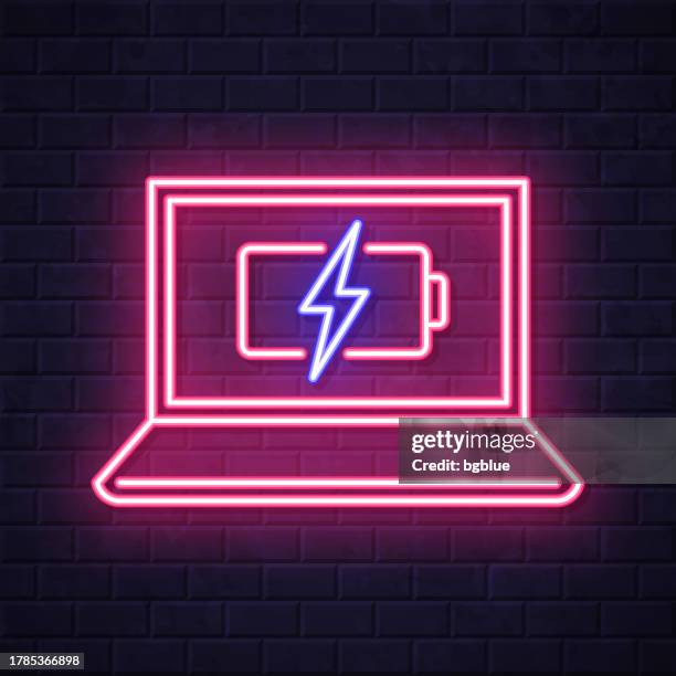 laptop with battery charge symbol. glowing neon icon on brick wall background - electrical meter stock illustrations