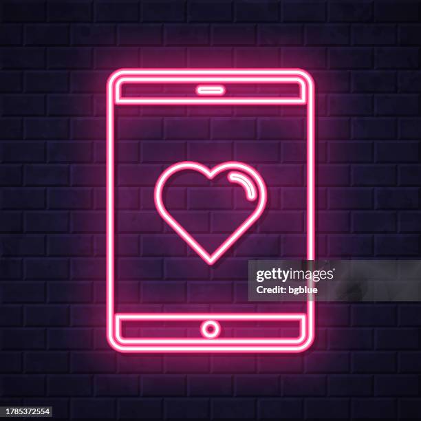tablet pc with heart. glowing neon icon on brick wall background - touch screen wall stock illustrations